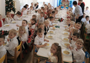 Dzieci siedzą przy dwóch, długich stołach podczas wigilijnego obiadu.