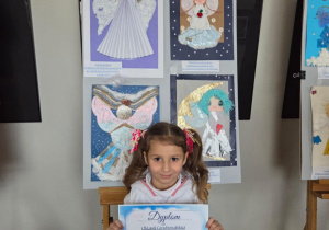 Oktawia z dyplomem w rękach na tle tablicy ze swoją pracą.