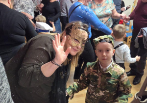 Babcia z Oskarem pozują do zdjęcia. Babcia ma na twarzy piękną wenecką maskę.