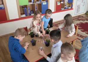 Sadzenie bratków przy stoliczkach pod nadzorem prowadzących warsztaty.