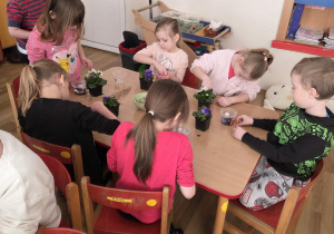 Sadzenie bratków przy stoliczkach pod nadzorem prowadzących warsztaty.