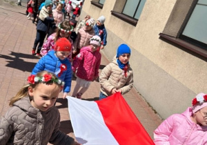 Dzieci maszerują pod pomnik demonstrując flagę.